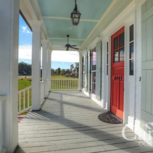 Customized Liberty Plan – Porch view with red door, sky-blue ceiling, green shutters, and wood rails