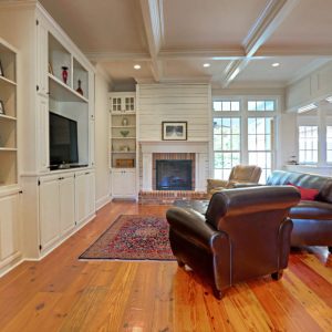 Customized Liberty Plan – Living room with fireplace, built-in entertainment cabinet, coffered ceiling, and paneled kitchen opening