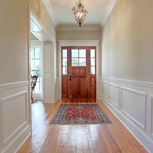Foyer with stained wood front door, heart pine flooring, chair rail, and paneled cased opening