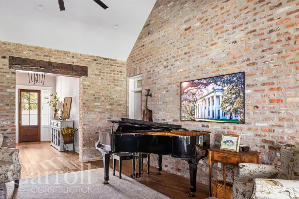 Living room with cathedral ceiling, antique beam, exposed brick wall, and grand piano near foyer