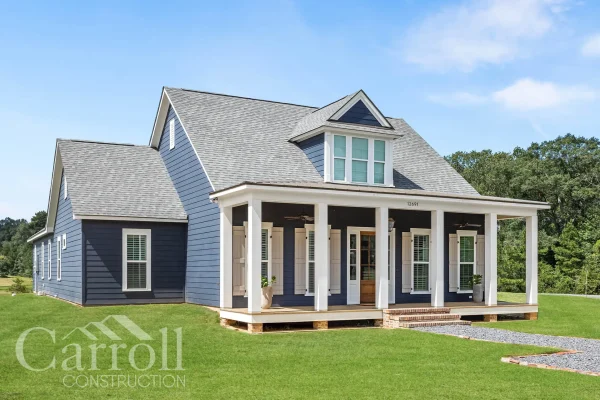 Angled view of Acadian-style farmhouse with wide front porch and traditional red door