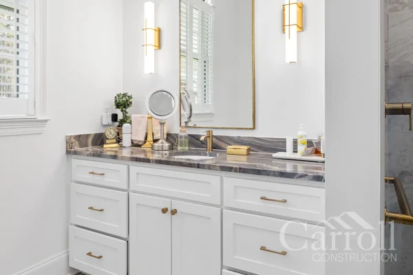 Bathroom vanity with brushed brass sconces, thin-line mirror, and matching brass faucet fixtures