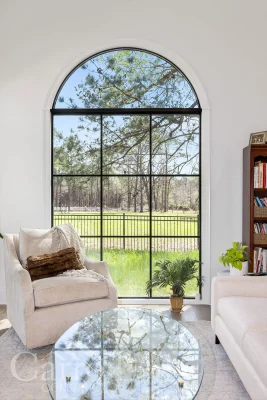 Large arched window in living room with outdoor view and accent chair in front