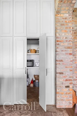Walk-in hidden pantry concealed behind paneled cabinet wall with one door open