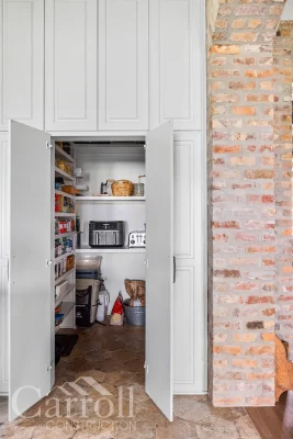 Fully open hidden pantry doors revealing walk-in storage space behind paneled cabinet wall